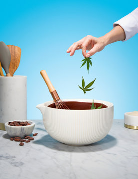 Chef Hand Adding Cannabis Leaves to Chocolate Mixing Bowl on Marble Countertop