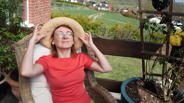 Smiling redheaded woman wearing straw hat sitting on balcony