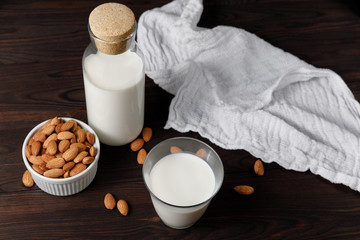 Almond milk in a glass and a glass bottle on dark wooden background