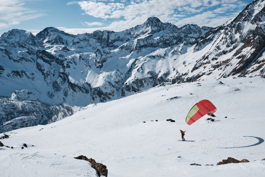 Man taking off with a paragliding wing and skis during a sunny winter day