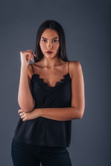 Naklejka premium Sensual studio portrait of a sexy woman standing with one arm crossed on a gray background
