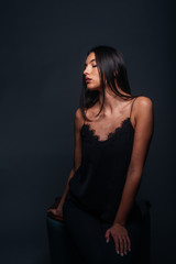 Fototapeta premium Beautiful sexy woman with straight black hair looking aside and being isolated on a dark background