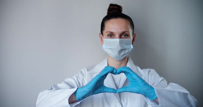 Woman with a medical mask and hands in latex glove shows the symbol of the heart. Doctor for the heart. Love to our pancreas. Love our medical professionals.
