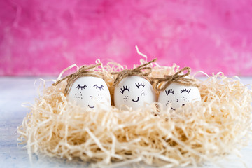 cute Easter chicken eggs with smiles in a nest on a pink background