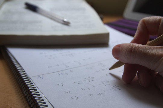 Someone does school homework in a notebook with the help of books and a tablet