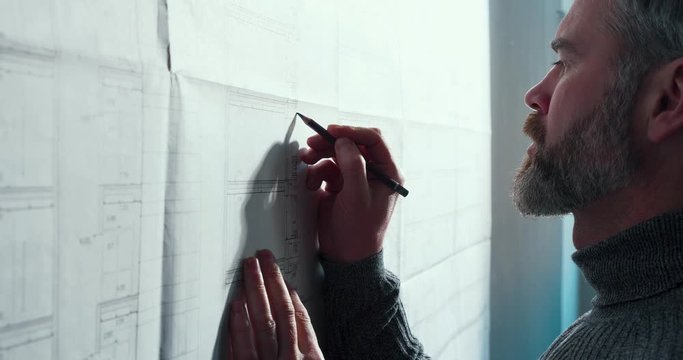 Close-up portrait of handsome man concentrated on work. Architect working in office with blueprints. Engineer sketching a construction project. Architectural plan. Business construction concept.