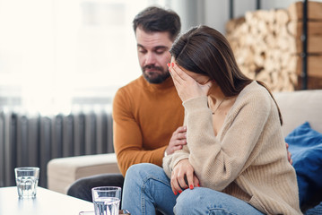 Young loving wife supporting her depressed husband during psychotherapy session with counselor,...
