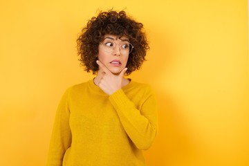 Young beautiful brunette woman wearing yellow sweater over yellow isolated background Thinking worried about a question, concerned and nervous with hand on chin.