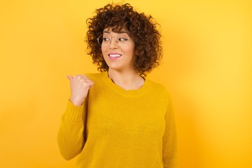 Portrait of charming arabian woman, promoter looking at copy space having advertisements isolated over yellow background.