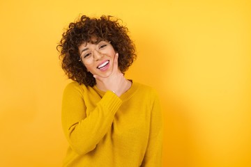 Young beautiful woman with curly hair wearing casual yellow sweater  looking confident at the camera smiling with crossed arms and hand raised on chin. Thinking positive.