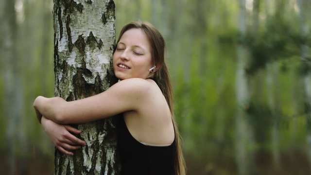 Young happy caucasian woman hugging the tree in the forest. Slow motion
