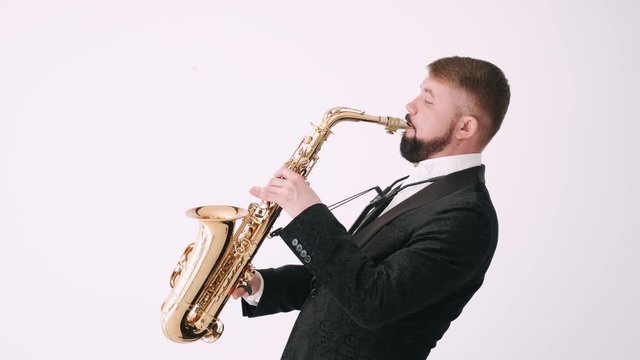 Man with beard is musician. Man holds saxophone. Person wears dark suit and white shirt.