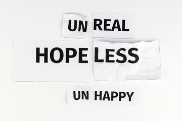 Words "unhappy", "hopeless, unreal" written on paper, is cut into two halves