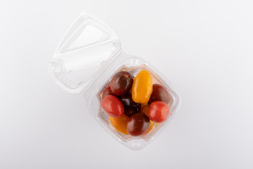 multi-colored tomatoes in a plastic box close-up on a white background