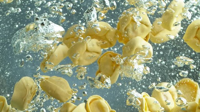 Throwing tortellini, pasta into boiled water in pot shooting with high speed cinematic camera at 1000 fps.