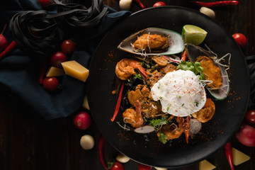 italian food background of black fettuccine spaghetti pasta with spiced seafood and poached egg in black palte on wooden table, selective focused