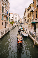 Fototapeta na wymiar Italy wedding in Venice. A gondolier rolls a bride and groom in a classic wooden gondola along a narrow Venetian canal. Newlyweds are sitting in a boat on the background of ancient buildings.