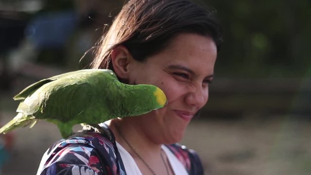 A cheeky green Caracas Parrotlet kisses then bites the cheek of a young tourist woman