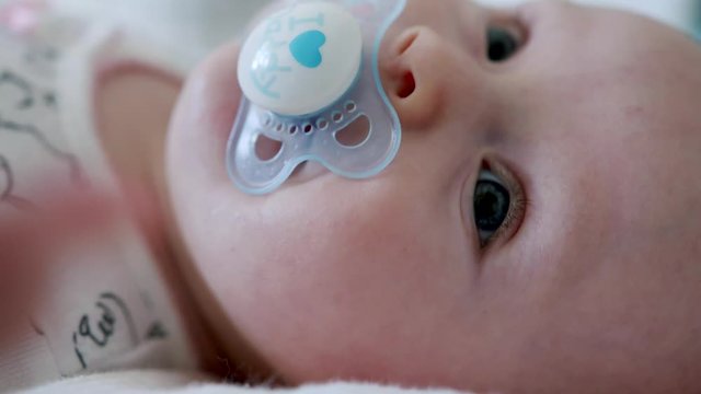 Close up adorable blue eyed baby sucks dummy as they wriggle on the floor