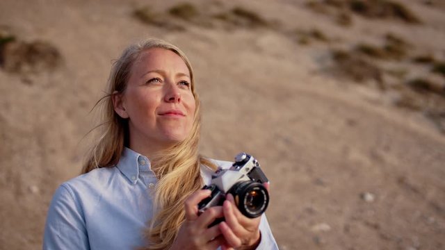 Close up shot of a pretty female photographer smiling and taking a photo with a film camera