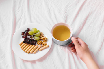 Top view of young woman drinking tea and having breakfast in her bed