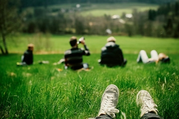 Group of people sitting on a hill with the rural view from it. Legs in sneakers at the foreground 
