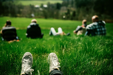 Group of people sitting on a hill with the rural view from it. Legs in sneakers at the foreground 