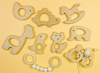 Close up cute nice small wooden baby teethers with different shapes on yellow background. Eco accessories for newborn, baby. Flat lay, top view