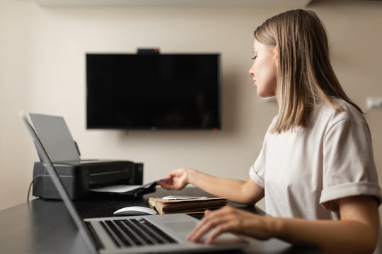 A Cute, Beautiful Girl Does Work From Home, Takes Out A Sheet Of White Paper From The Printer During Quarantine.