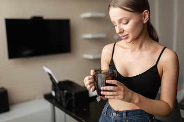 smiling girl freelancer does the work from home holds a mug with tea while relaxing during a break from work. Home workplace