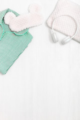 Comfort neo-mint color pajama, headphones, fluffy cushion and sleeping eye mask on white wooden background on white wooden background. Accessories for quiet sleep. 