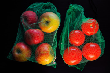 Bright red apples and tomatoes in green eco bags close up on a dark table
