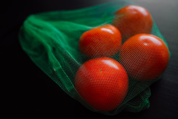 Bright red tomatoes in green eco bag close up on a dark table