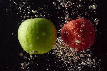Green and red apple fruits falling into water and splashing against black background