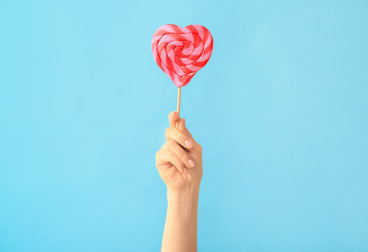 Hand with sweet lollipop on color background