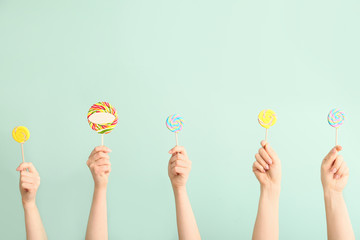 Hands with sweet lollipops on color background
