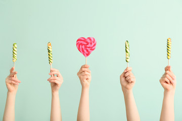 Hands with sweet lollipops on color background