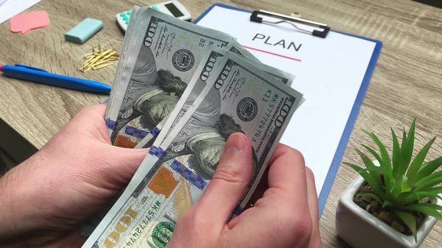 Plan, man counts 100 dollar banknotes at a wooden table