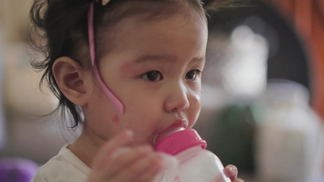 Asian baby girl sucking bottle of milk in hands, small kids development, toddler drinking milk from bottle, Infant formula milk, one asian good looking cute female