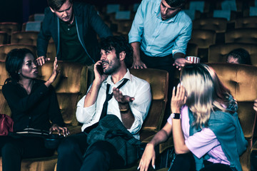 Annoying man talking on the mobile phone at the movie theater people in cinema is angry him