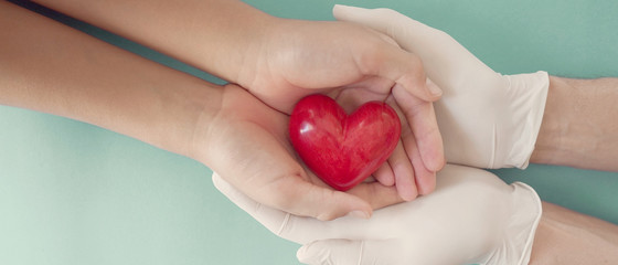 Doctor hands with medical gloves holding child hands and red heart, health insurance, donation,...