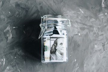 One hundred dollar banknotes in a glass bank on a gray concrete background.