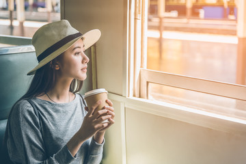 Happy young Asian cute woman sitting, holding coffee cup and looking outside the window train. Travel summer and holiday concept.