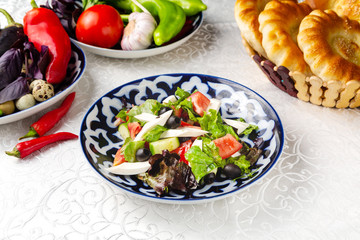 Salad of fresh vegetables, tomatoes, cucumbers, greens. Traditional oriental dish. On a plate on a table in a restaurant.