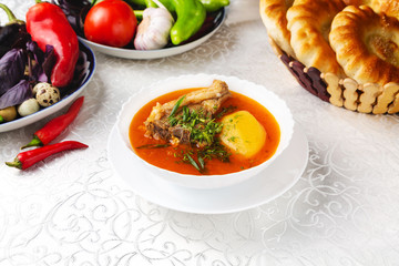 Red soup with meat, vegetables and herbs. Traditional oriental dish. On a plate on a table in a restaurant.

