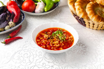 Red soup with meat, vegetables and herbs. Traditional oriental dish. On a plate on a table in a restaurant.
