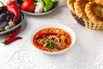 Red lagman soup with noodles, vegetables and herbs. Traditional oriental dish. On a plate on a table in a restaurant.
