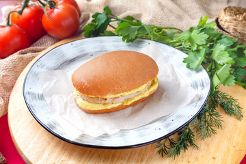 Sandwich with cutlet and cheese on a plate on a background of vegetables and herbs