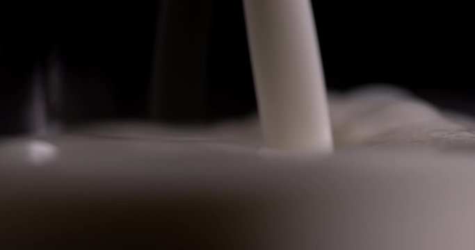 Macro milk is pouring into a glass on a black background in slow motion