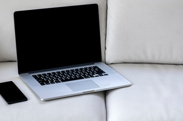 Mockup black screen laptop with black screen smartphone on white leather sofe in living room.